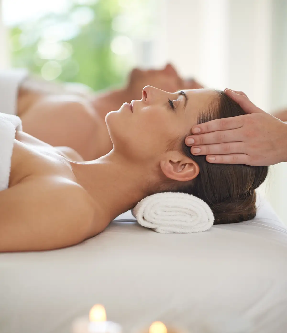 Junges Paar genießt einen Verwöhntag. Ein Ehepaar liegt zusammen auf Massagetischen und erhält Kopfmassagen – ein Muss in jedem Wellnesscenter.