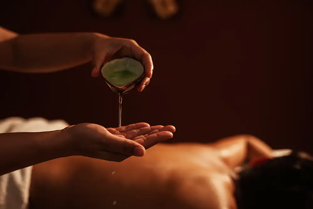 Masseur gießt Aromaöl auf seine Hand, um den Rücken des Kunden zu massieren. Entspannung: Junger männlicher Kunde erhält eine Aromatherapie-Massage von einer Masseurin in einem Spa-Salon.